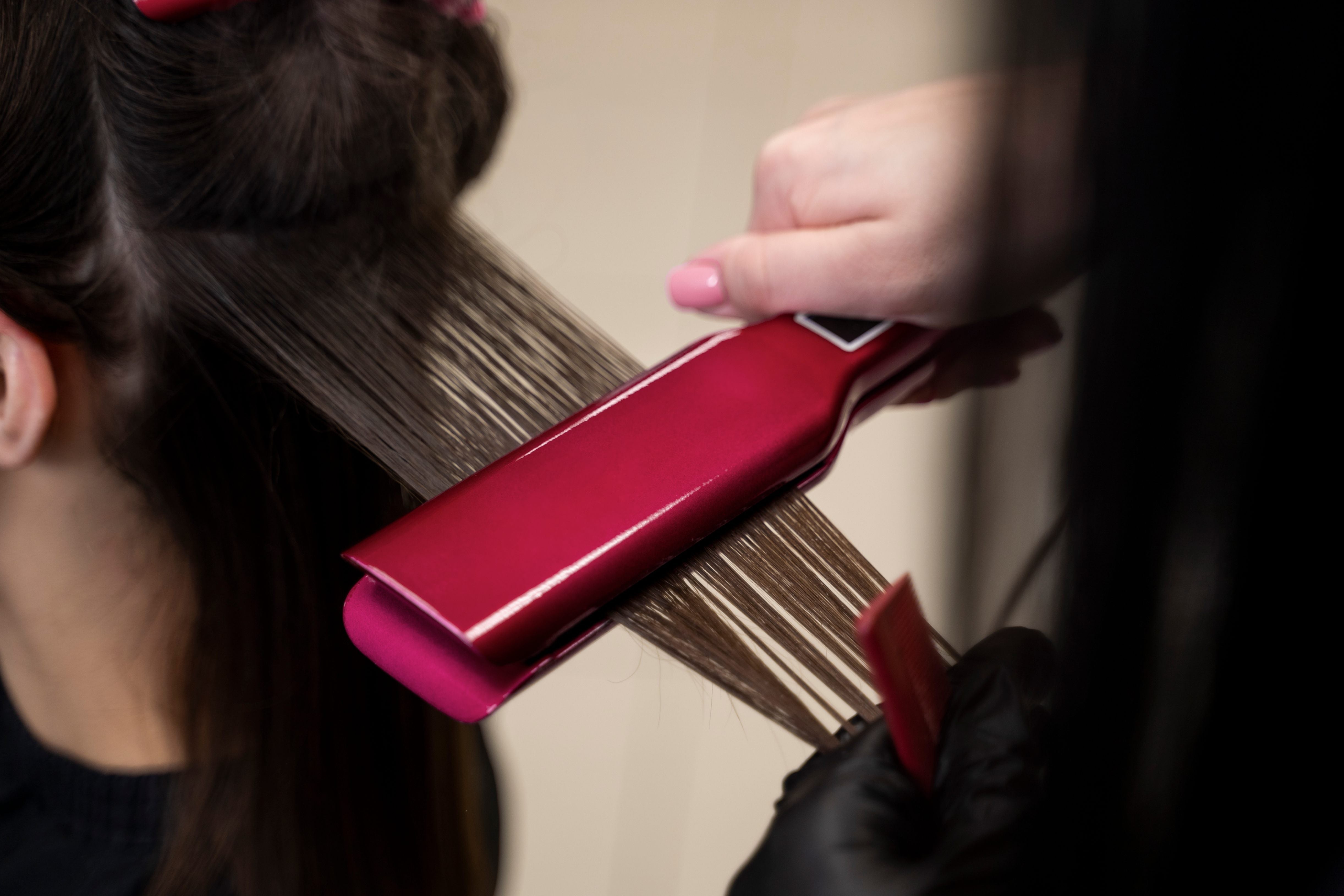 Hair stylist using flat iron to straighten extensions in salon.