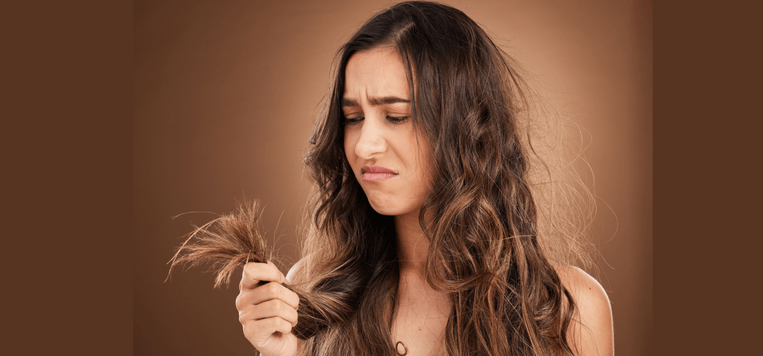 Woman looking disappointed at dry, frizzy split ends in her long brown hair.