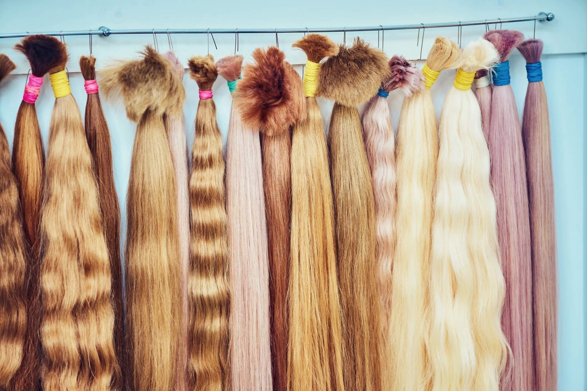 Various natural-looking human hair bundles in different shades and textures displayed on hooks, representing options for custom wigs and hair toppers for thinning hair.