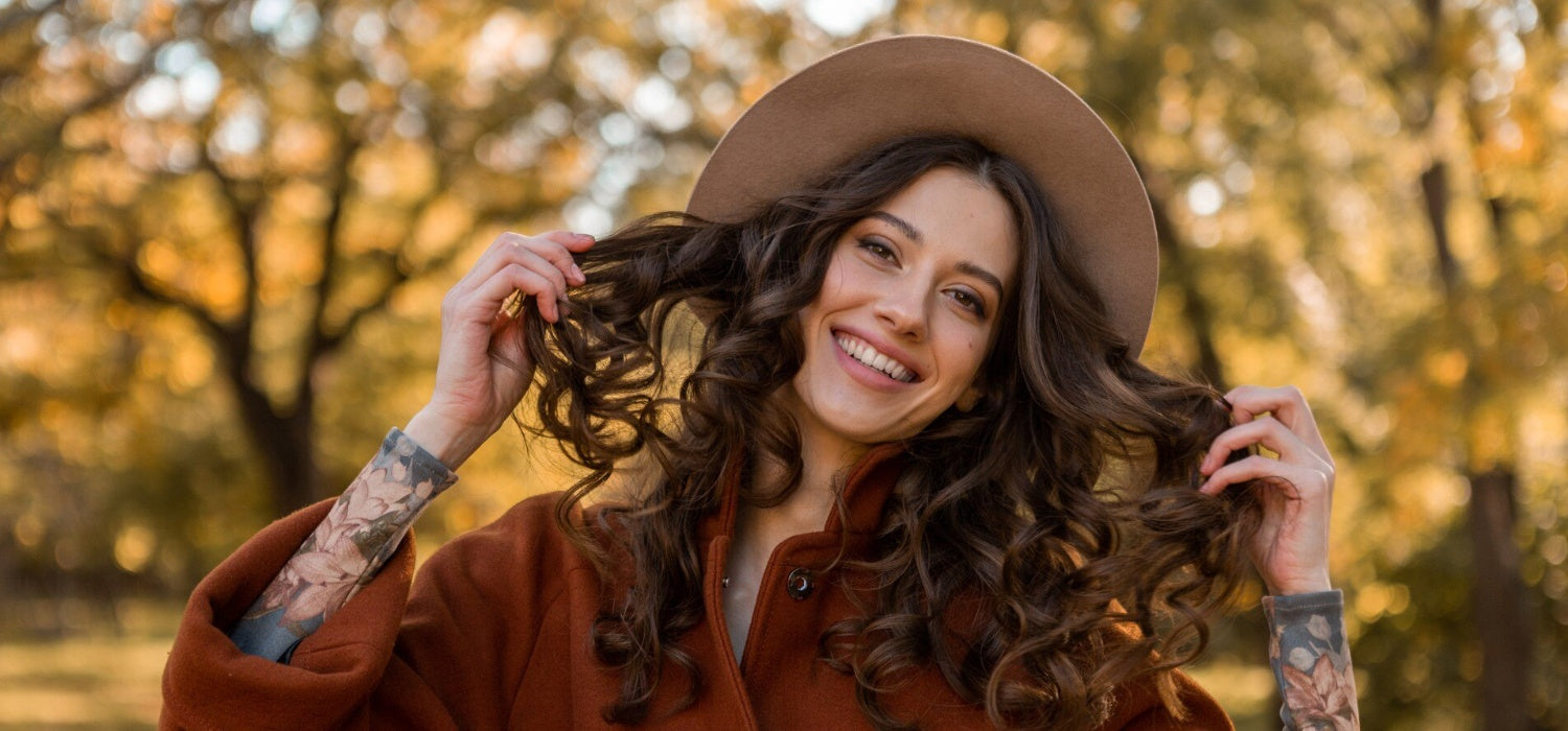 Woman with soft curls smiling outdoors in fall, showcasing effortless Thanksgiving hair ideas.